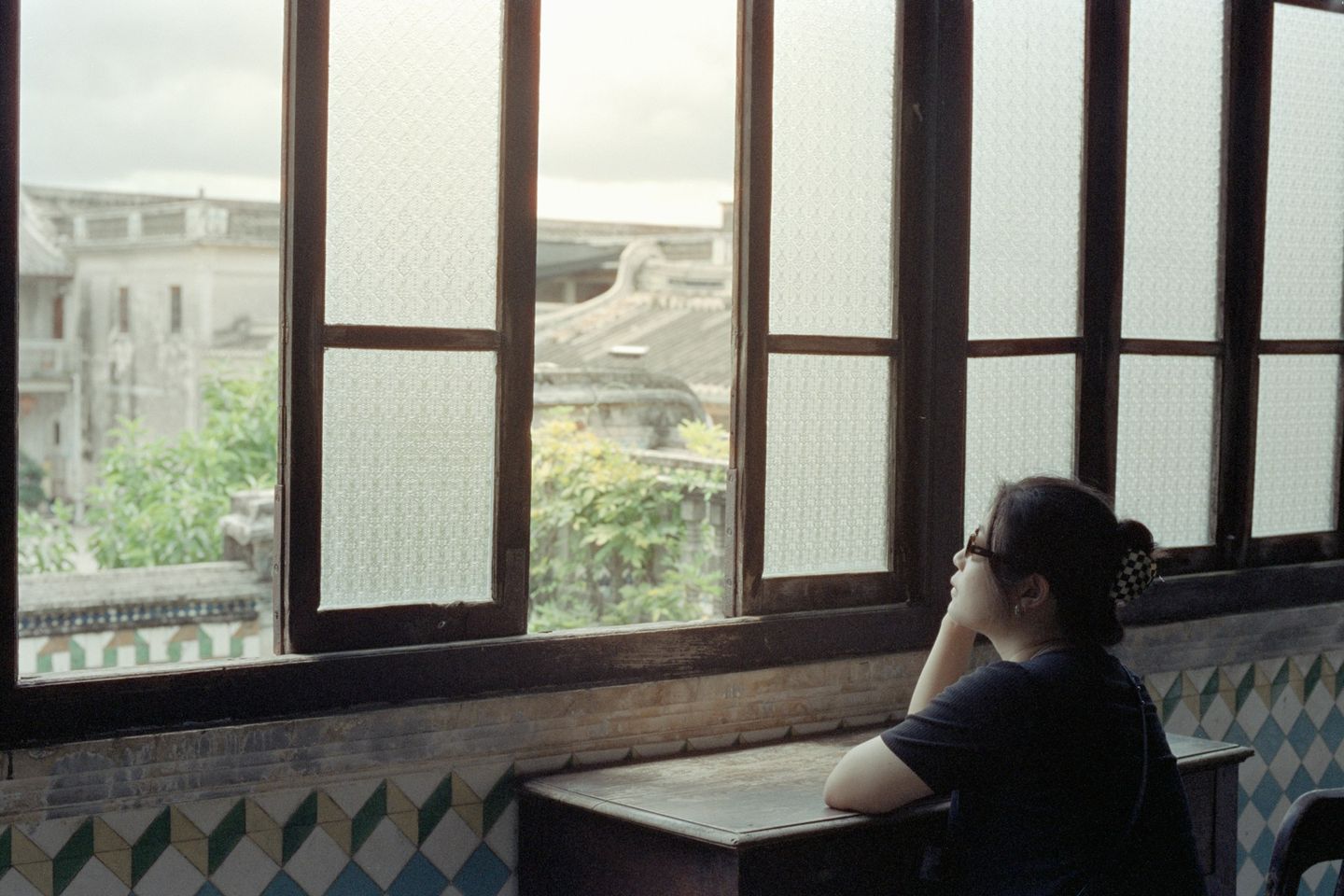 A woman pausing quietly beside a window in daylight